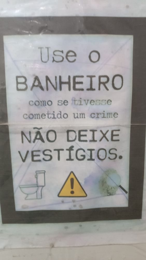 Placa de banheiro escrito: USENO BANHEIRO COMO SE TIVESSE COMETENDO UM CRIME NÃO DEIXE VESTÍGIOS 