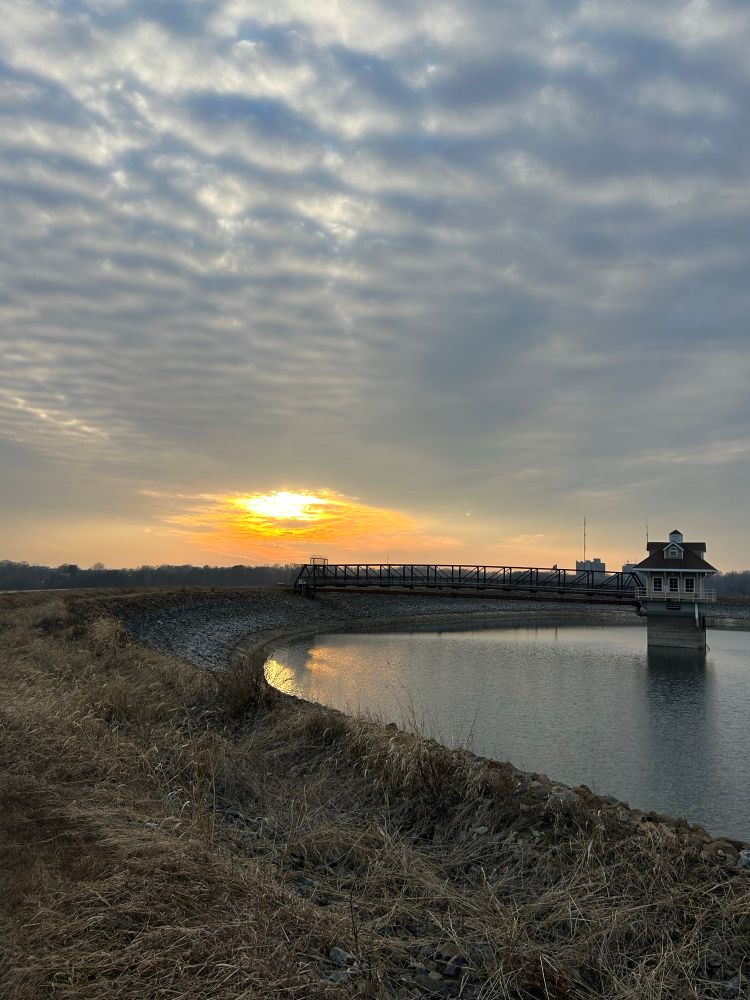 sun breaking through clouds over a reservoir