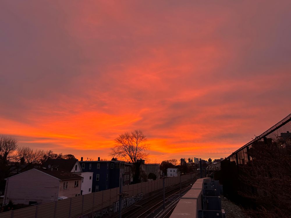 bright orange-pink clouds over a railroad track heading toward the Boston skyline.