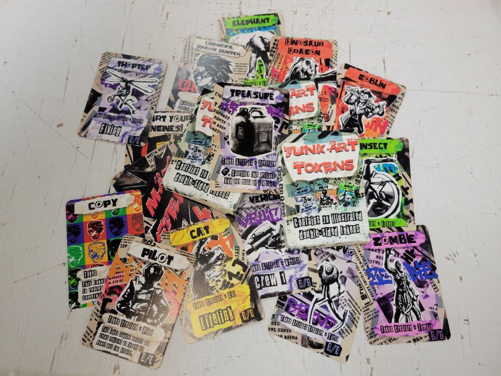 A messy spread of the tokens in the token pack. The tokens are rendered in a cut and paste magazine collage style.  The tokens are:
Colorless 1/1 Pilot with "Can crew vehicles and saddle mounts as though its power was 2 greater."
White 1/1 Cat with Lifelink
Black 2/2 Zombie
Red 4/4 Dinosaur Dragon with Flying
Red 1/1 Goblin
Green 3/3 Elephant
Green 1/1 Insect
Colorless Artifact 1/1 Servo
Colorless Artifact 1/1 Thopter with Flying
Colorless Artifact Treasure
Colorless Artifact 3/2 Vehicle with Crew 1
Colorless Chandra, Spark Hunter Emblem that reads "Whenever an artifact enters, this emblem deals 3 damage to any target."
Colorless Copy Token
"Start your Engines!" Helper card