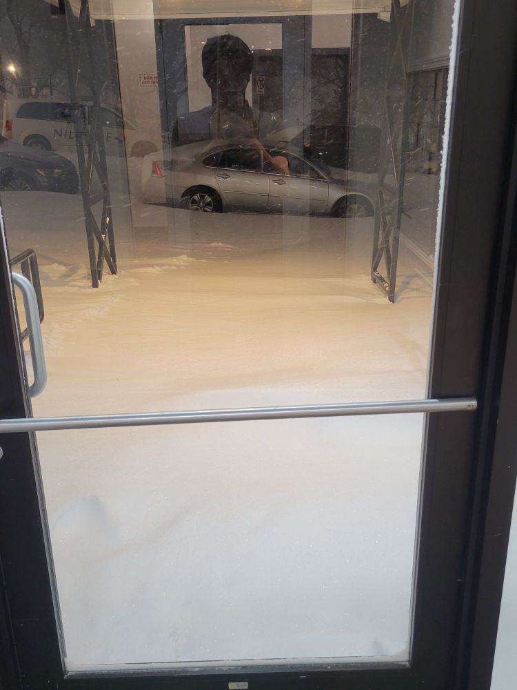 A look outside a clear, glass door.  There is a massive pile of snow blocking the way.