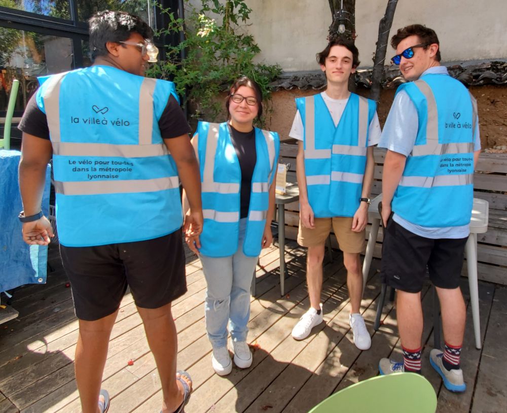 Photo des 4 étudiant·e·s portant le gilet bleu de La Ville à Vélo, dont 2 de dos
