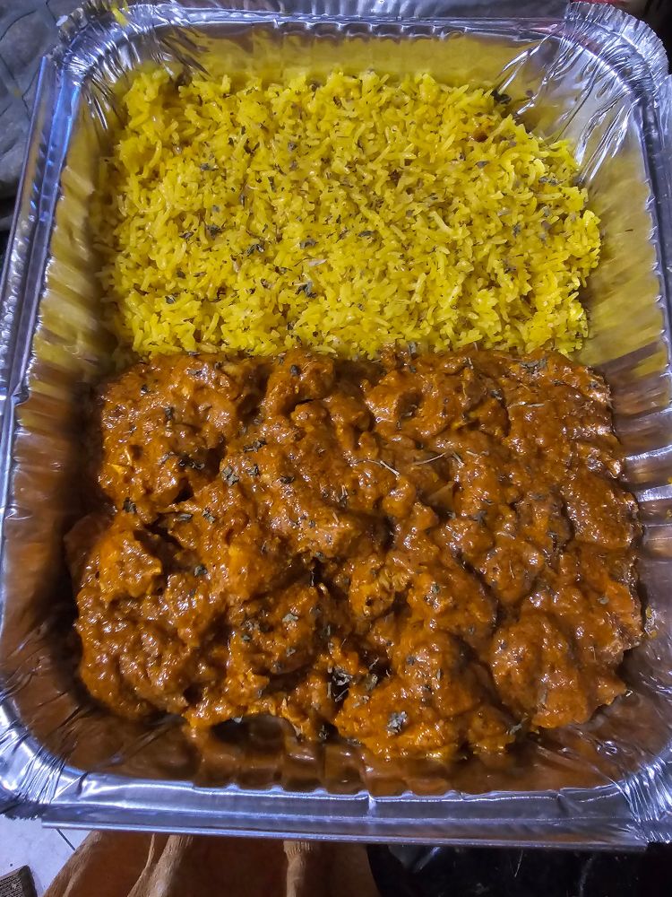 Aluminum pan of bright yellow saffron rice in one half and chicken tikka masala in the other half