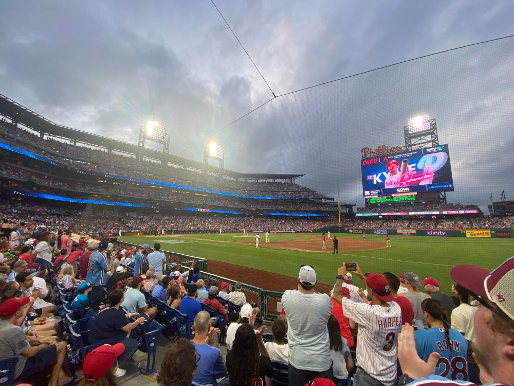 Phillies game with evening lights and fans standing as Kyle Schwarber comes up to bat. 