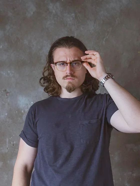 Une photo du même Joshua Weissman, mais pas convaincu. Il tient ses lunettes avec sa main gauche et fronce ses sourcils.