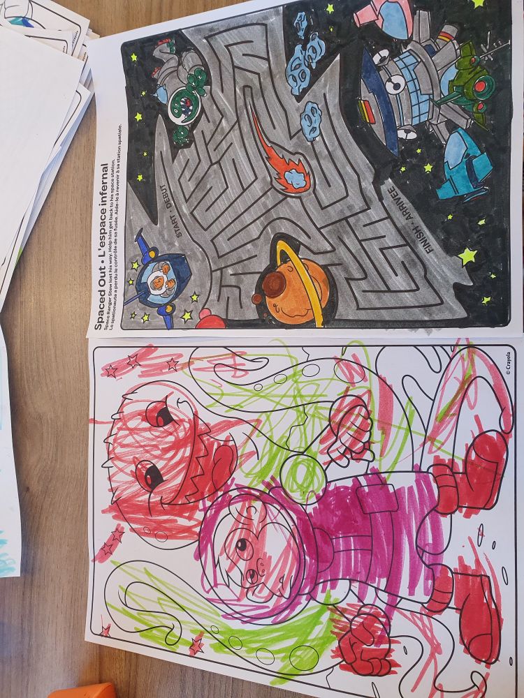 Two colouring pages. On the left is a chimp in a spacesuit being menaced by a tentacle alien. The chimp is red, in a pink spacesuit with red gloves and boots. The alien has green tentacles and a red head and eyes. The colouring is scribbly (average for a 5 year old). On the right is a maze with an astronaut in a small spaceship on the top left as the start and a space station at the bottom right as the goal. It had been coloured in by an adult (me) and is mostly grey and black.