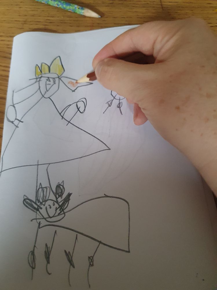 An adult hand is holding a small brown pencil, colouring in the hair of a royal in a triangular dress. There is a four-legged creature at the bottom of the page