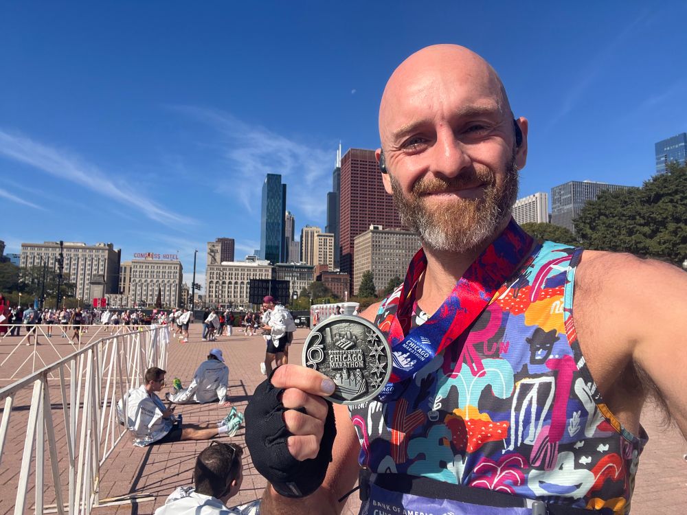 Bald bearded man holding a marathon finisher medal