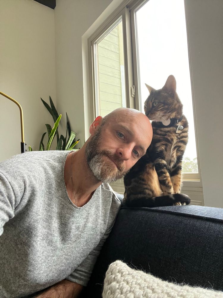 Bald bearded man on a couch with a striped cat 