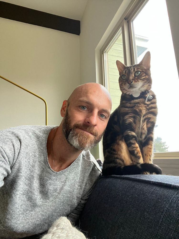 Bald bearded man on a couch with a striped cat 