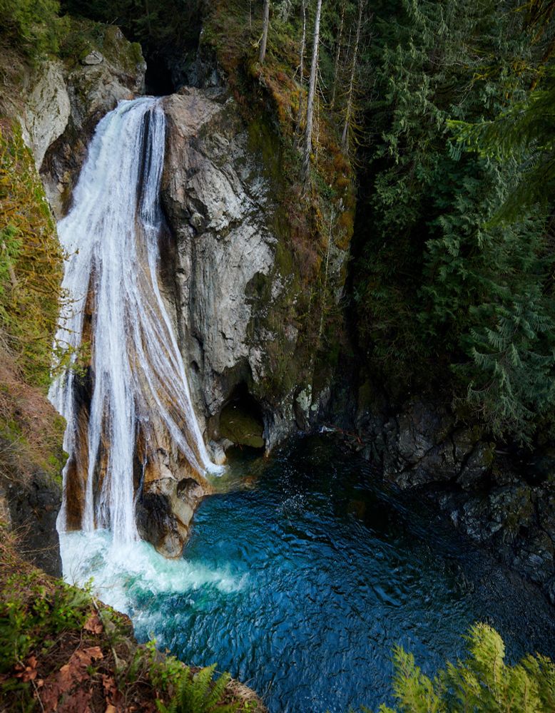 A tall waterfall streams down a rockface into a sapphire blue pool. Nikon D850, 24-70