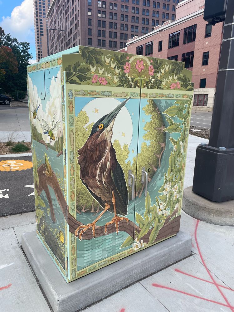 A colorful and detailed design covers a municipal street utility box, featuring a bird and other creatures native to Minnesota's stretch of the Mississippi River