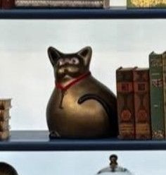 A shot of the Big Brother bronze and bulbous cat figurine giving side eye called Louise with a red ribbon around her neck that has a gold old style fancy key hanging from it
