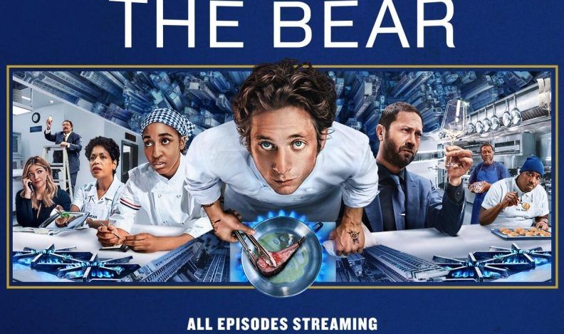 Promo image for TV series THE BEAR. The cast is in the kitchen, standing upright. Carmy is in the center of the frame, but he alone was photographed from above, so it looks like he's flying toward the camera like Superman.