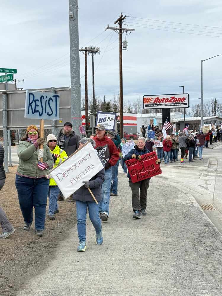 People carrying signs march along the side of the Sterling Highway in Soldotna, Alaska, on Saturday, April 5, 2025.