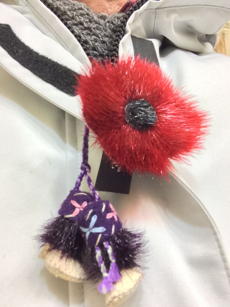 A red sealskin poppy along with miniature kamiik are pinned to a coat. 