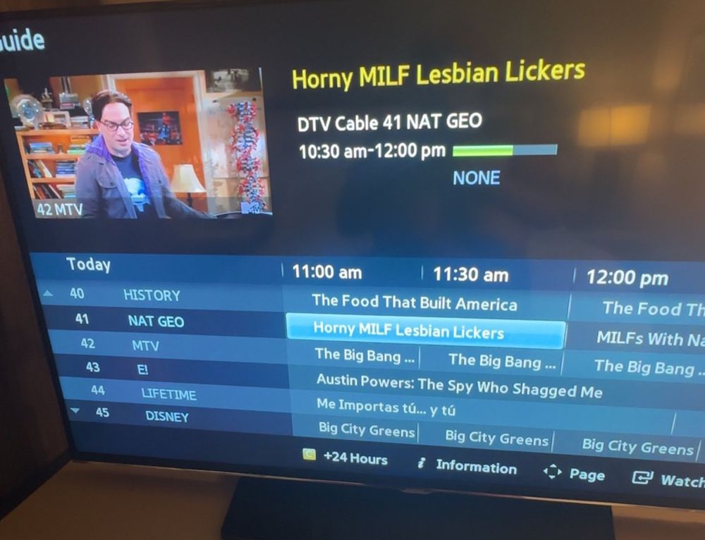 Image of a cable TV programming guide interface displayed on a television screen. The guide shows a dark blue background with white text and multiple program listings organized in a grid format.
Main Program Display (top center):
	•	Title: “Horny MILF Lesbian Lickers”
	•	Channel: DTV Cable 41 NAT GEO
	•	Time: 10:30 am-12:00 pm
	•	Progress bar showing approximately 30% complete (green portion) with remaining time in blue
	•	Rating: NONE
Preview Window (top left):
Small video thumbnail showing a scene from The Big Bang Theory featuring a man with glasses wearing a purple hoodie, standing in an apartment with bookshelves and laboratory equipment visible in the background. “42 MTV” appears in the bottom left corner of this preview.
Channel Lineup (left side):
	•	Channel 40: HISTORY
	•	Channel 41: NAT GEO (currently selected/highlighted in blue)
	•	Channel 42: MTV
	•	Channel 43: E!
	•	Channel 44: LIFETIME
	•	Channel 45: DISNEY
Program Grid (center/right):
Time slots displayed: 11:00 am | 11:30 am | 12:00 pm
Programming shown includes:
	•	History Channel: “The Food That Built America”
	•	NAT GEO: “Horny MILF Lesbian Lickers” (highlighted in light blue)
	•	Multiple channels showing “The Big Bang Theory” episodes
	•	Lifetime: “Austin Powers: The Spy Who Shagged Me”
	•	Disney: “Big City Greens”
Navigation Bar (bottom):
Icons and options for “+24 Hours,” “Information,” “Page,” and “Watch”​​​​​​​​​​​​​​​​