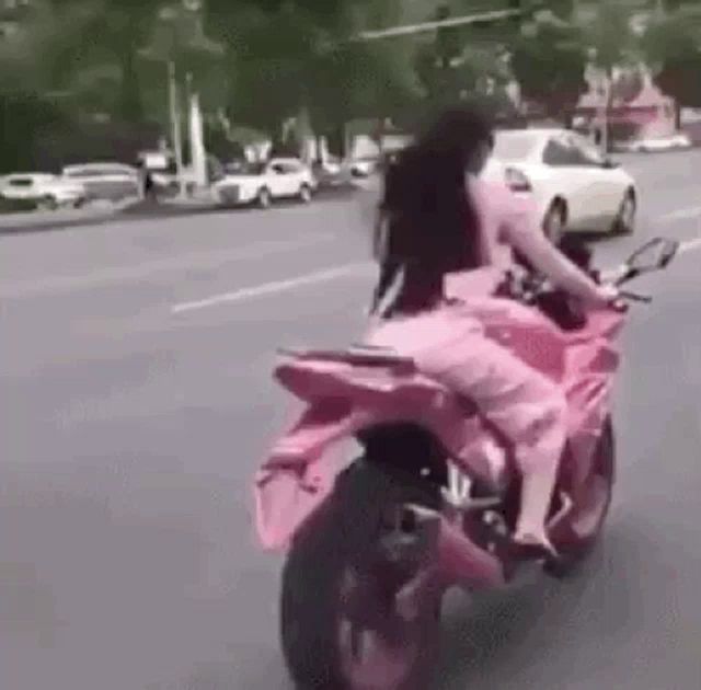 a woman in a pink dress is riding a pink motorcycle on a street .