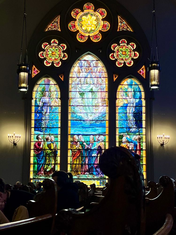 Tiffany stained glass window of the disciples looking up at the transfiguration of Jesus with angels around them 