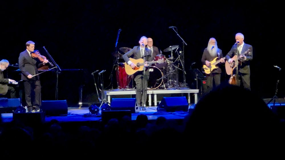 Lyle Lovett singing on stage with his acoustic band