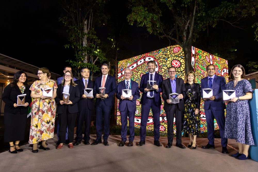 A group of formally dressed people holding awards in front of colorful illuminated artwork.