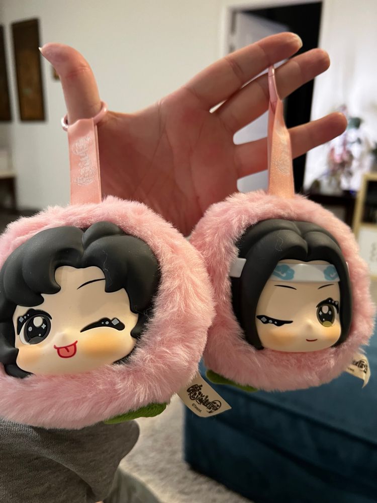 Wangxian fruit plushie keychains, these are peaches with the head of Lan Zhan winking in one and the head of Wei Ying winking sith his tongue out in the other.