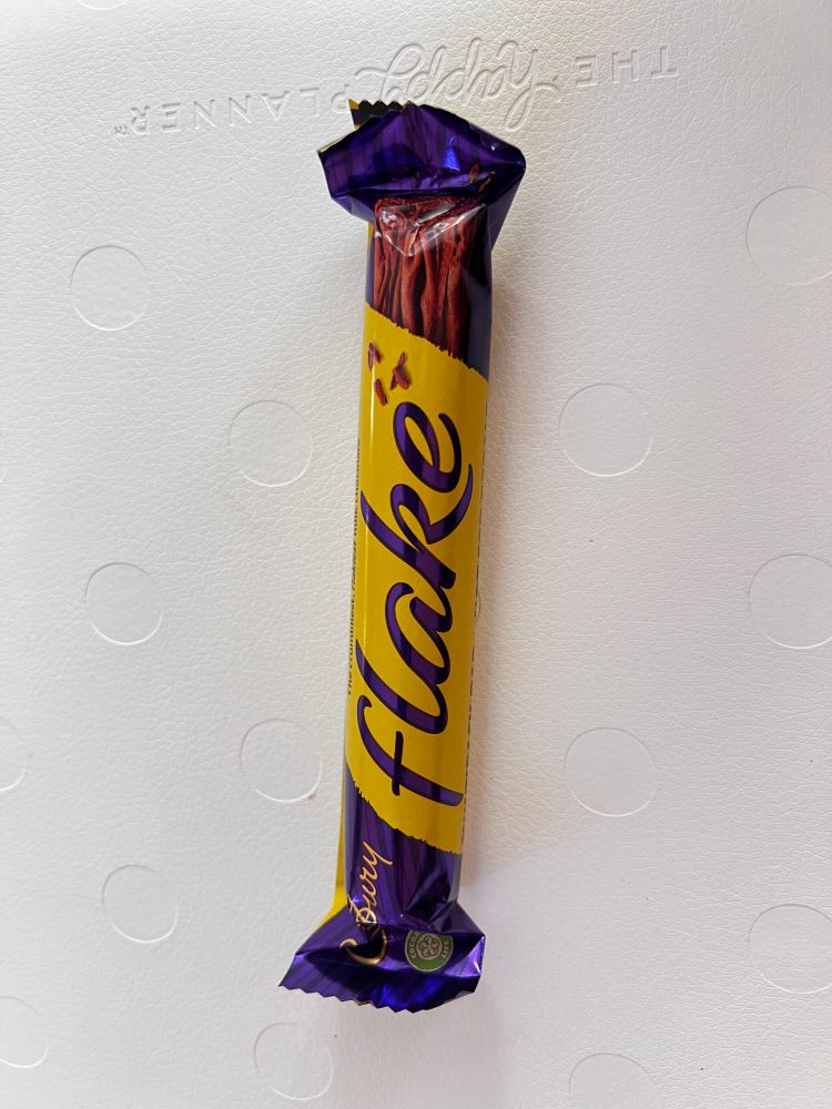 A photo of a Cadbury Flake bar. The wrapper is purple at the ends and yellow in the middle. The name of the bar is j purple script over the yellow. 