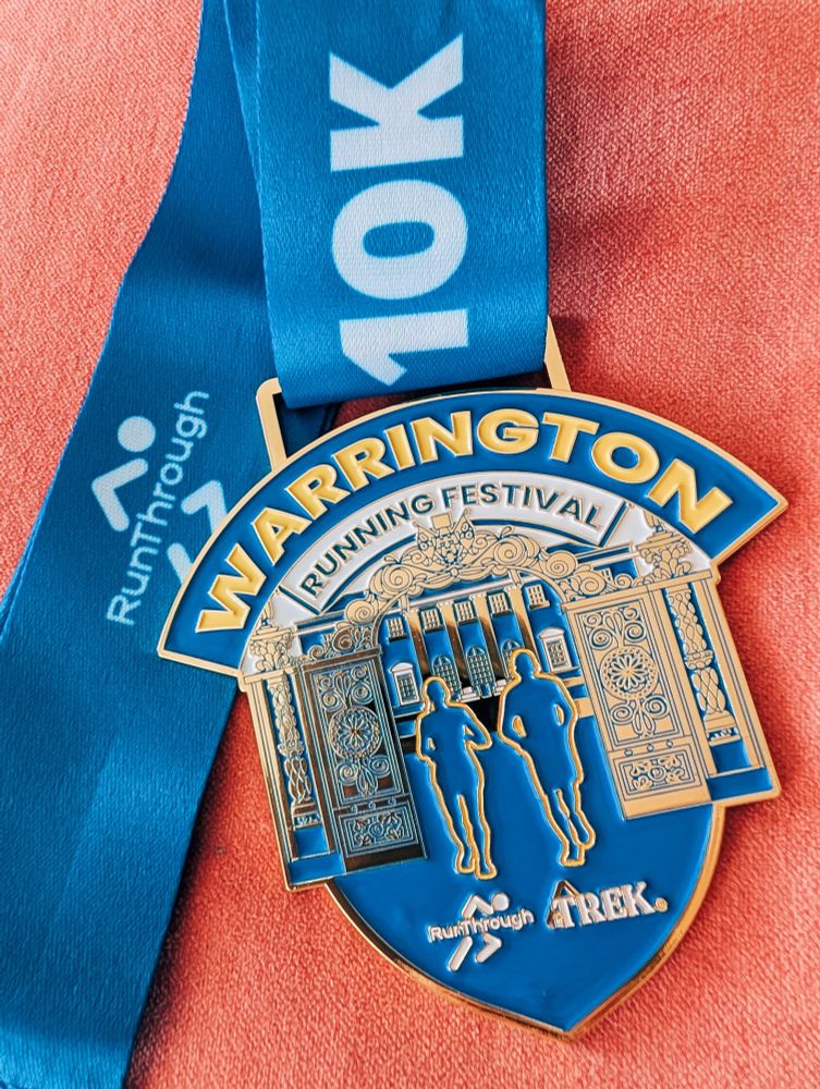 The 10K finishers medal that shows two silhouetted runners going through Warrington's iconic Golden Gates 