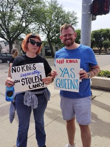 A photo of me and my friend with our signs. Hers reads, “ no kings, especially on stolen land” and my reads, “ no kings, YAS QUEENS”