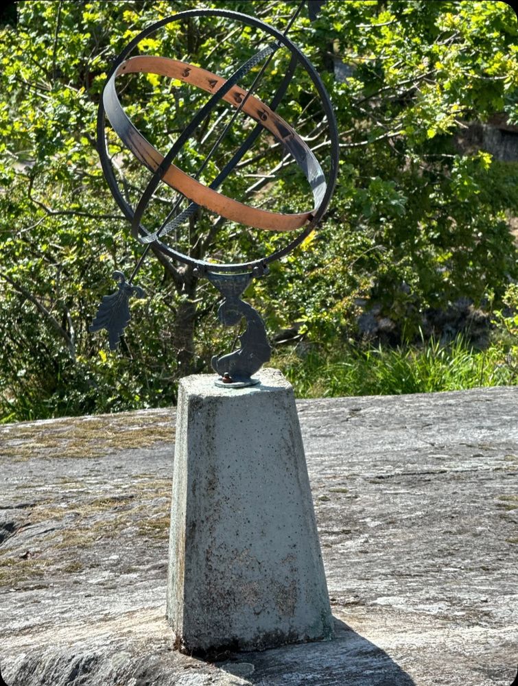 A sundial is fixed in bedrock and has dense greenery in the background