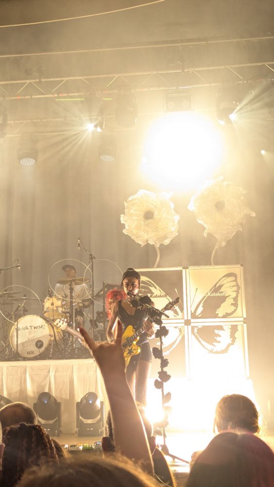 Amy Love of Nova Twins stood at a microphone stand covered in black roses singing and playing guitar