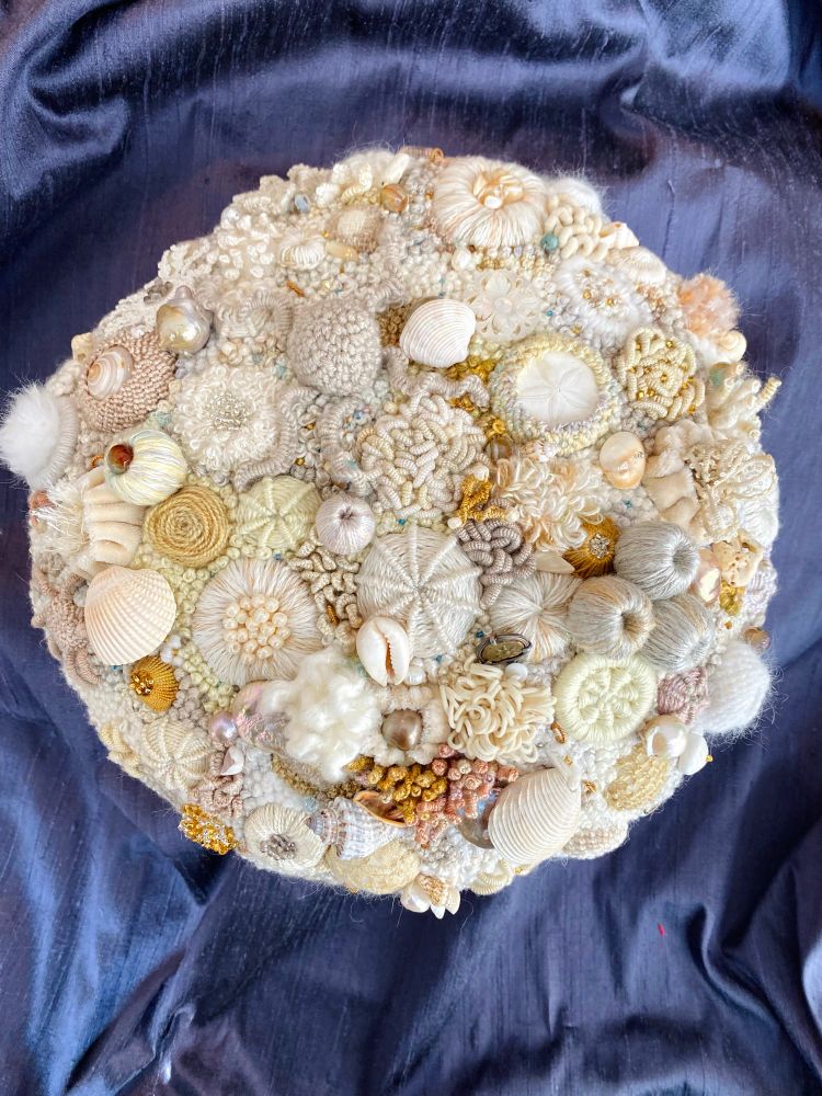 A hand embroidered circular bleached coral reef with natural elements shown on a dark background.