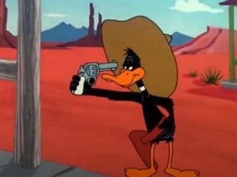 Daffy Duck pointing a revolver directly at his face in a wild west town. He is wearing a holster and a cowboy hat.