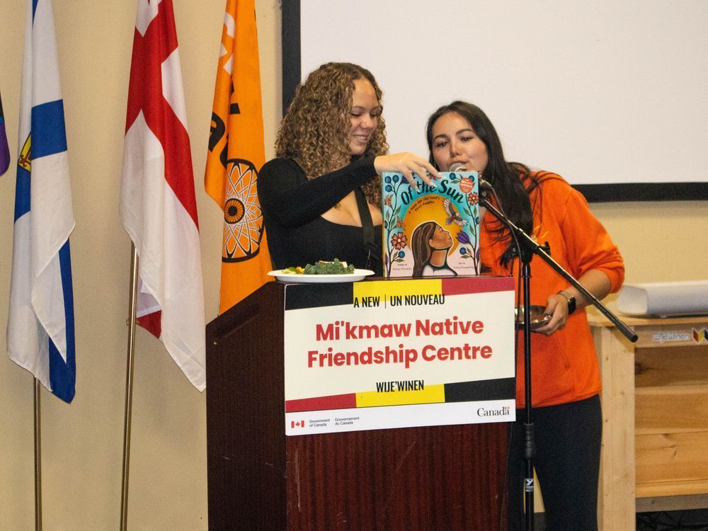 Two young women at a podium at the Mi’kmaw Native Friendship Centre hold up a children’s book while presenting during an event.