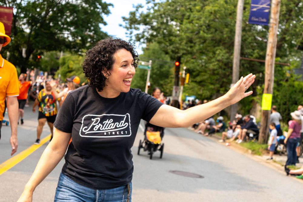 A close-up of Claudia Chender waving mid-parade, with excitement and energy in the air.