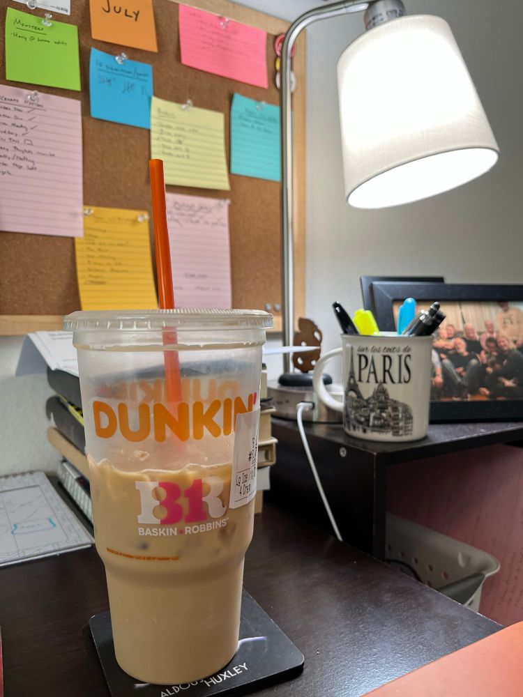 Picture of a Dunkin iced coffee in front of my writing goals pegboard. 
