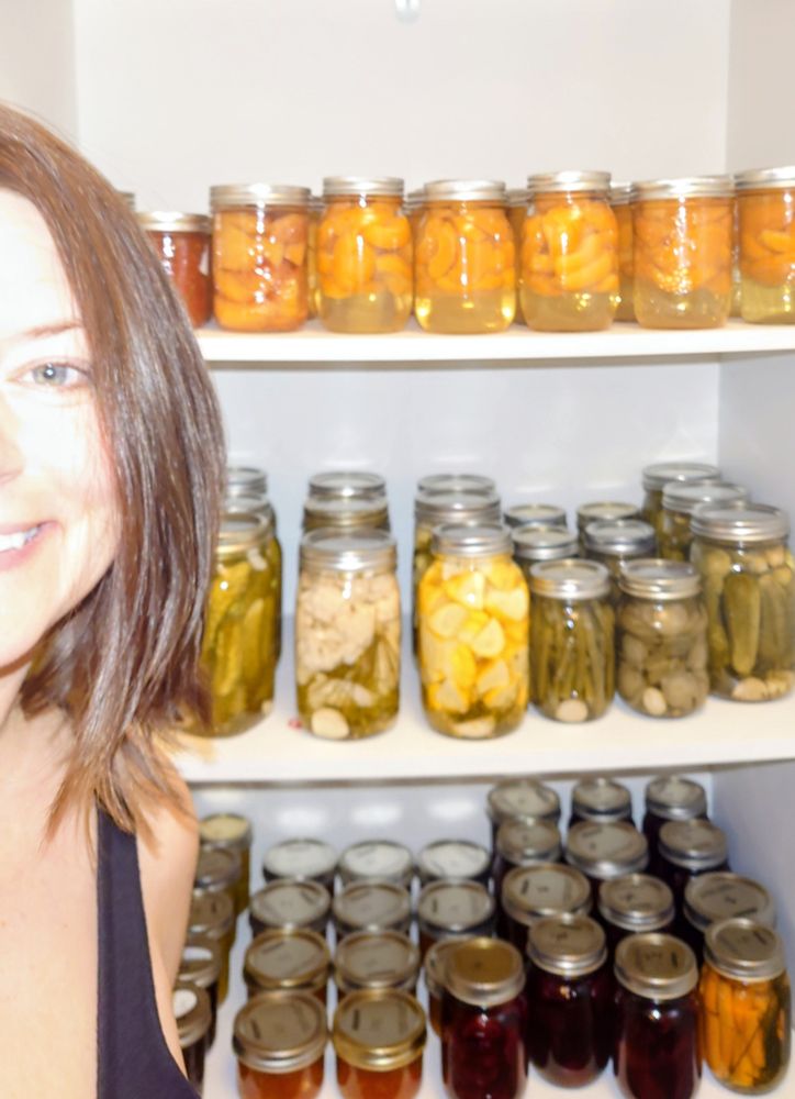 It's me, smiling, proudly in front of neatly organized shelves filled with home-canned goods in glass jars — peaches, pickles, cauliflower, beans, and beets — glowing in warm tones of gold, green, and red.
