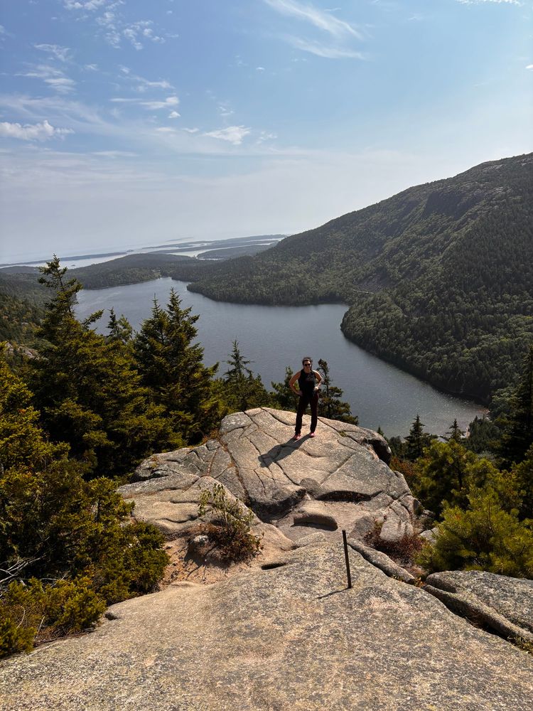 A sassy curvy gal with hands on her hips on a big rock with water, trees around and behind her. #slay