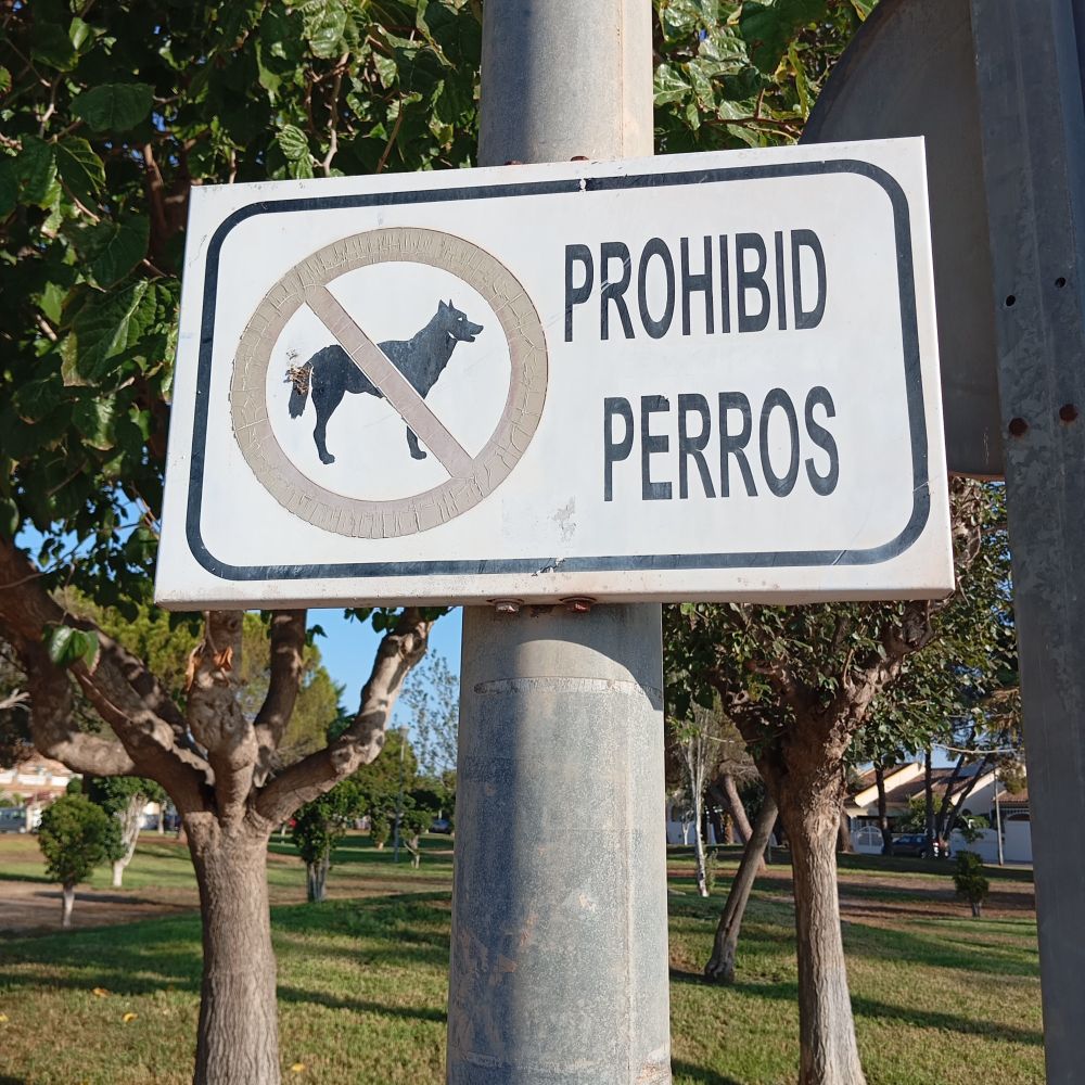 Señal de un parque en la que aparece la silueta de un perro bajo la señal de prohibido y la frase «prohibid perros».