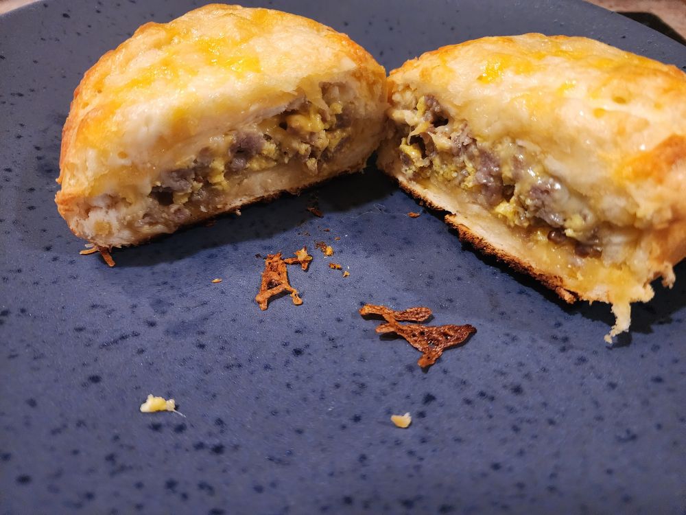 Cross section of homemade breakfast hot pocket on blue plate. Maple sausage, egg, cheese and toasted cheese on top.
