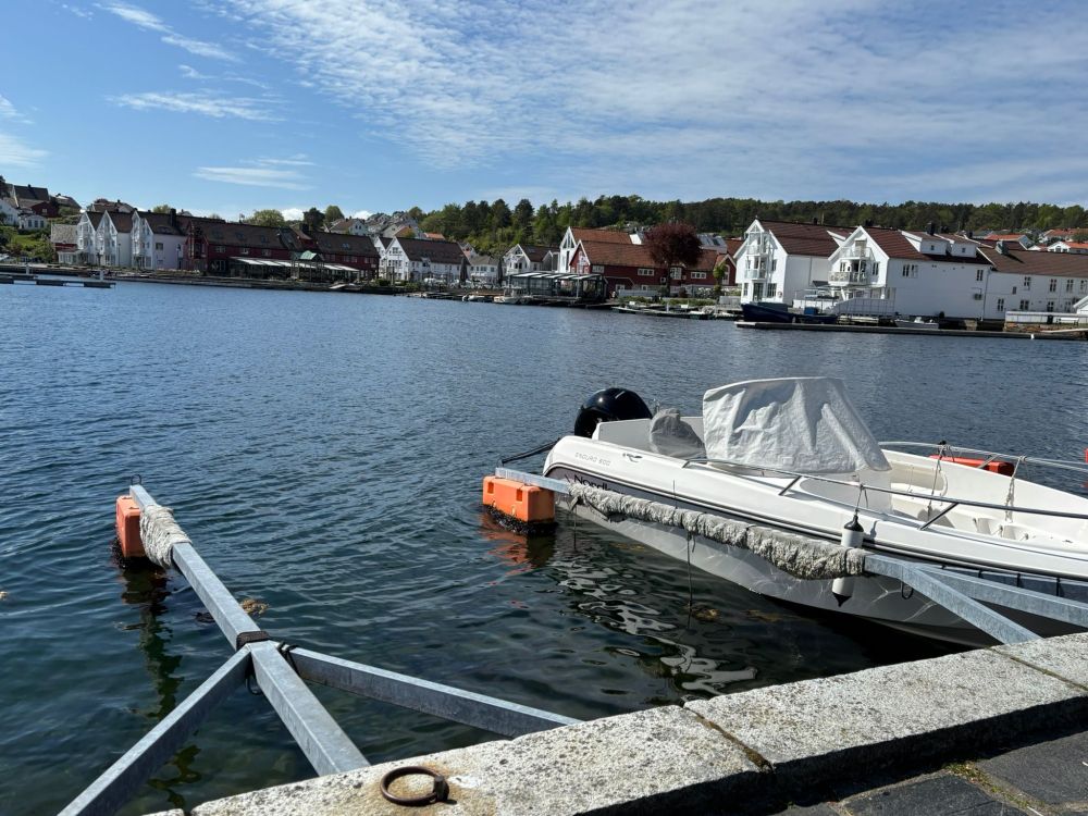  📸meins
Im Vordergrund ein Bootssteg mit einem kleinen Motorboot. Im Hintergrund am unteren anderen Ufer mehere Häuser. 