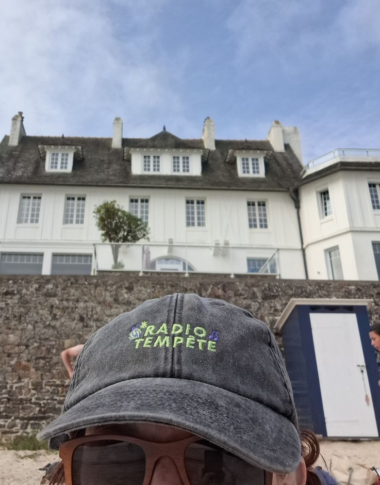 Ciel bleu, grande maison blanche de richous, mur en pierres et au premier plan, ma casquette Radio Tempête sur ma tête.