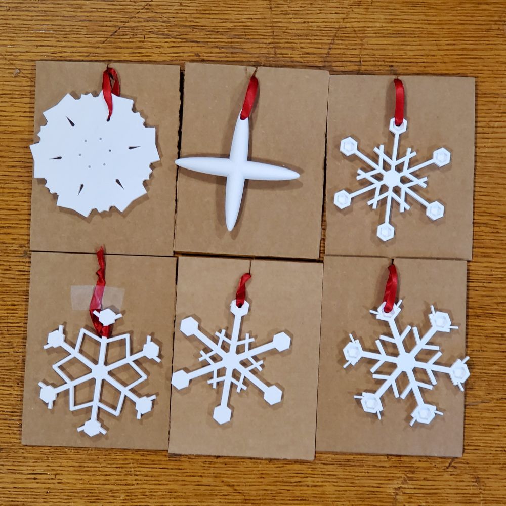 white 3d printed snowflakes students created using Tinkercad Codeblocks code and mounted onto cardboard squares with red ribbon