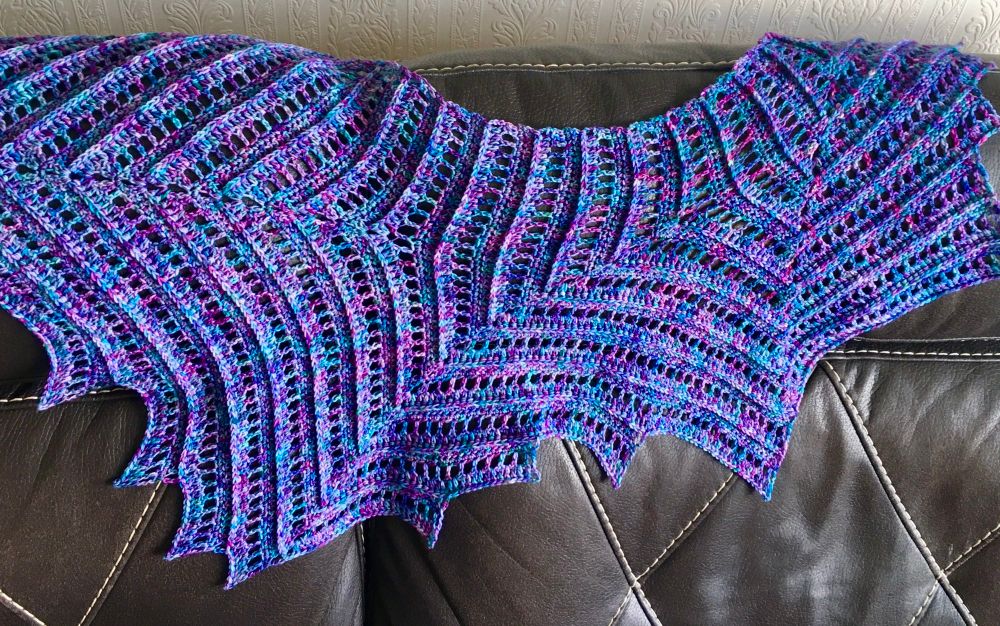 Duinen by Morben Design is an asymmetric shawl in the shape of a dragon wing. Features a ribbed texture, and spikes on one end. 

Yarn is merino, and hand-dyed by Giddy Yarns in her “Kings and Queens” colourway from her Narnia collection, which is a jewel-toned Purple speckled with pinks, blues and greens. 