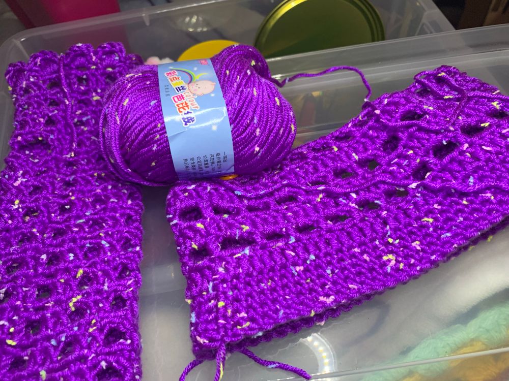 along one side is a fingerless mitt crocheted with an open square mesh stitch. next to it is the beginning of beanie in the same yarn with a similar but more rectangular mesh stitch. 