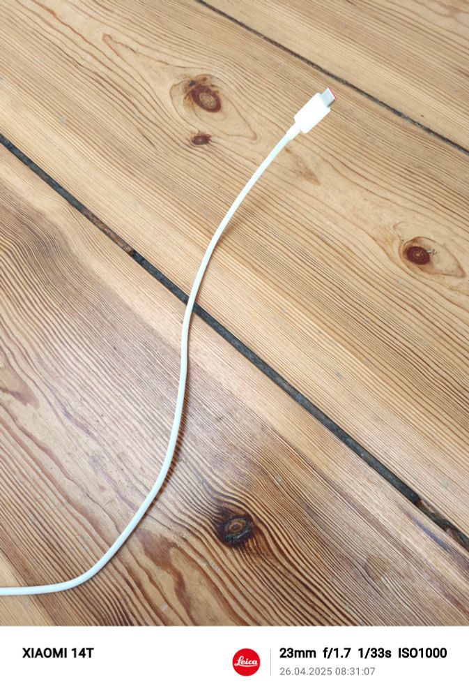 Holzboden, Ladekabel von Handy liegt darauf, weiss, Stecker ragt etwa 4 cm nach oben, hat was schlangenförmiges