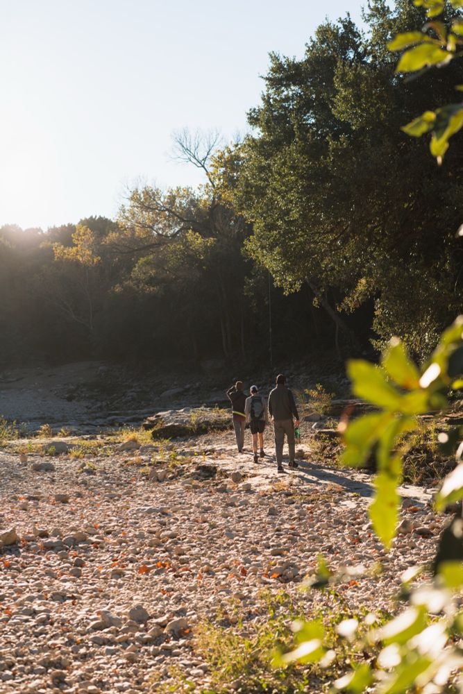 Three hikers hike in a dried creek bed in Austin Texas. 