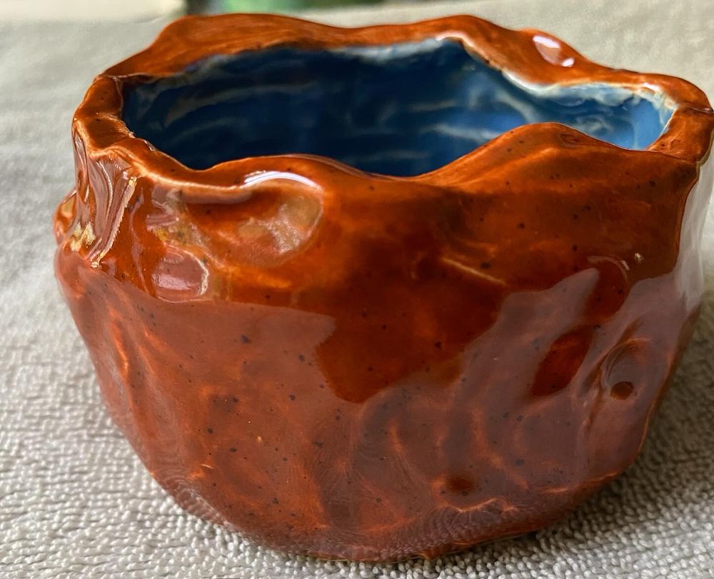 A textured dark orange bowl, roughly carved, with a blue interior 