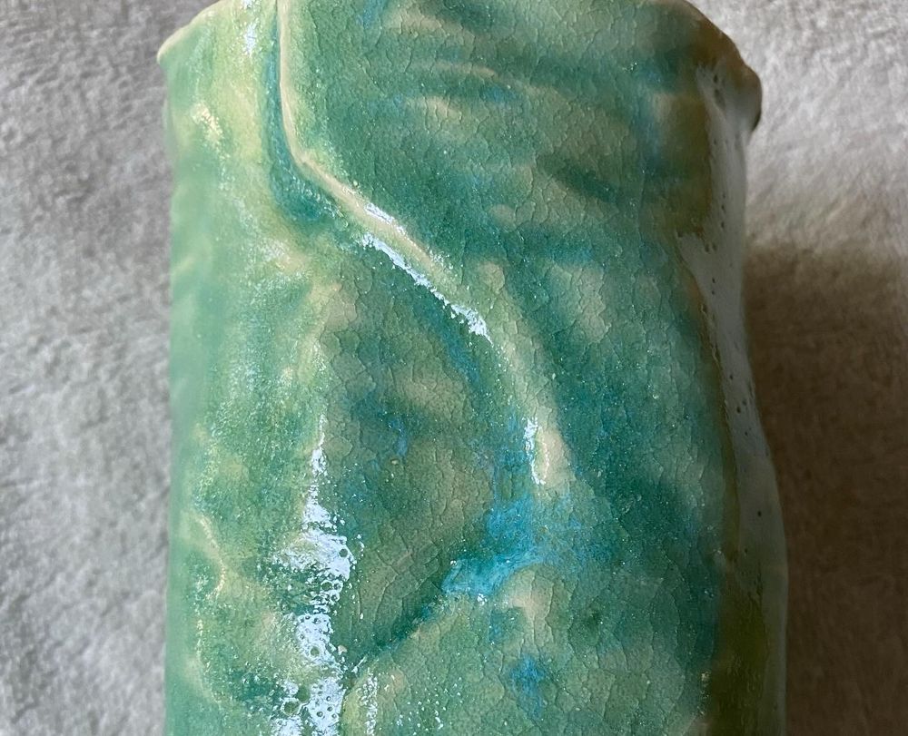 A crackled turquoise green texture on the side of a ceramic cylinder