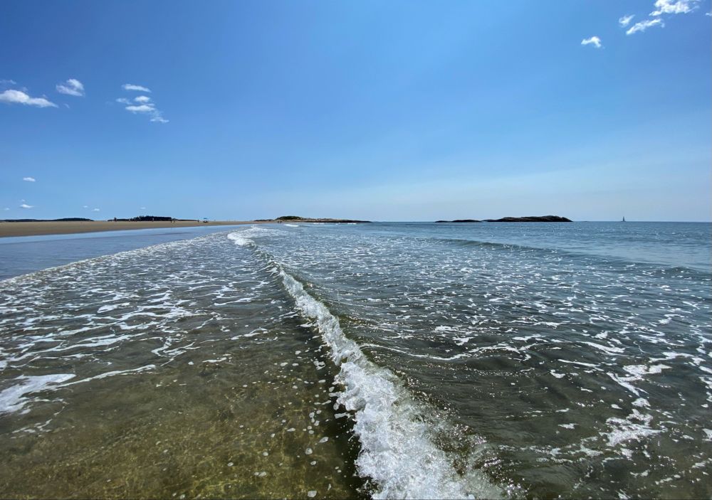 Small ocean wave from a few feet into the water with islands and sand in the far distance 